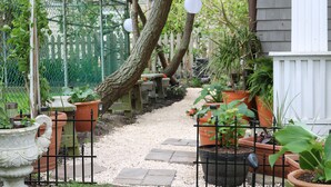 Un chemin de jardin bordé de plantes en pot, un banc en bois et une clôture en métal.