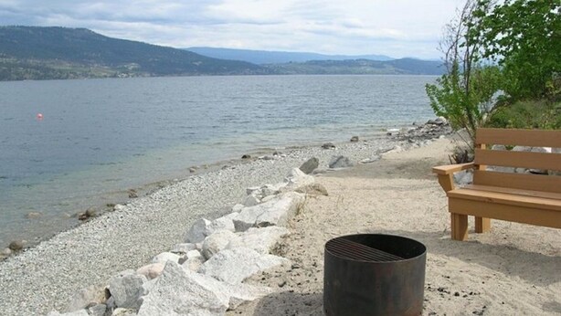 A lakeside setting with a wooden bench and a metal grill on a rocky shore. - Private Lake View Cottage with amenities for everyone! (Kelowna)