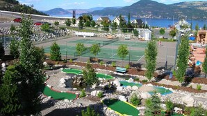 A tennis court complex with multiple courts, a small building, and a scenic view of a lake and mountains. - Private Lake View Cottage with amenities for everyone! (Kelowna)