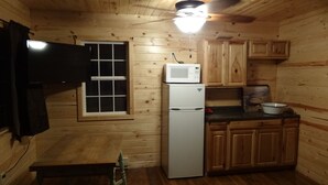 A compact kitchen with wooden walls, a refrigerator, a microwave, and a small dining table.