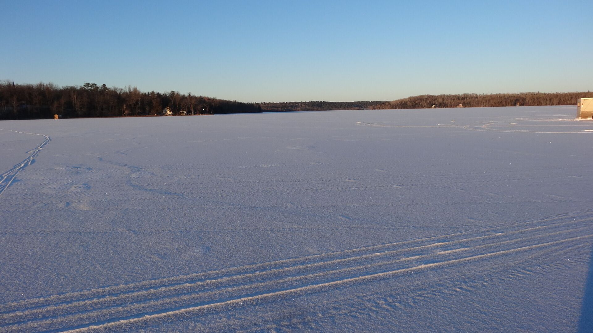 Eine weite, offene Schneefläche mit Spuren von Reifen und einem Gebäude in der Ferne.