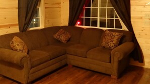 A corner sectional sofa with patterned cushions in a room with wooden walls and a window with curtains.