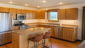 Una cocina moderna con armarios de madera, electrodomésticos de acero inoxidable, encimera de granito y un taburete de bar.