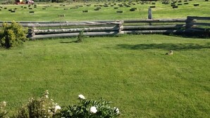 Paisaje rural con una terraza de madera al frente, un campo con fardos de heno y montañas en la distancia.