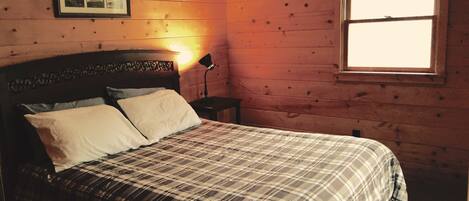 A room with a bed, a nightstand, a lamp, and a window.