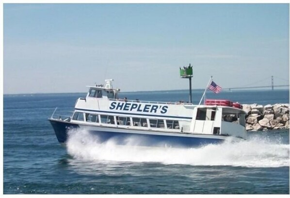 Un bote llamado SHEPLER'S avanza entre las aguas, con una costa rocosa y un puente al fondo.