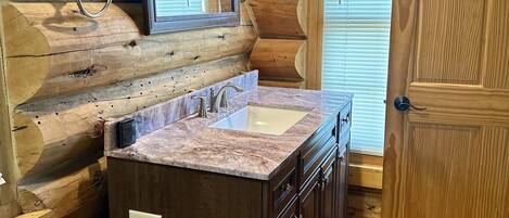 A log cabin bathroom with a marble sink, wooden cabinets, and a large mirror.