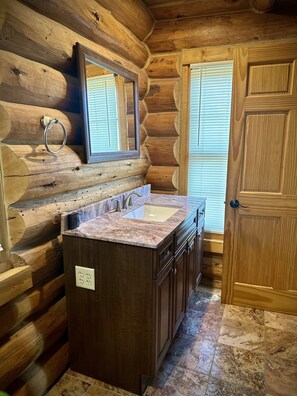 Une salle de bain rustique, aménagée dans une cabane en rondins, avec un lavabo en marbre, des meubles en bois et un grand miroir.