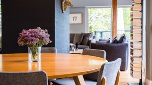 A dining area with a round wooden table, chairs, a vase with flowers, and a bookshelf with books. - Maple View Medlow Bath, Blue Mountains (Medlow Bath)