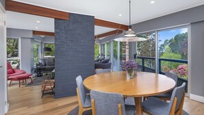 A modern dining area with a round wooden table, grey upholstered chairs, and a hanging pendant light. - Maple View Medlow Bath, Blue Mountains (Medlow Bath)