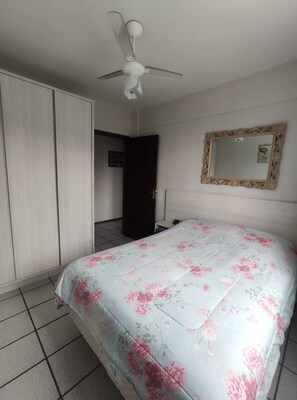 Une chambre à coucher avec un lit, une armoire, un ventilateur de plafond et un miroir au mur.