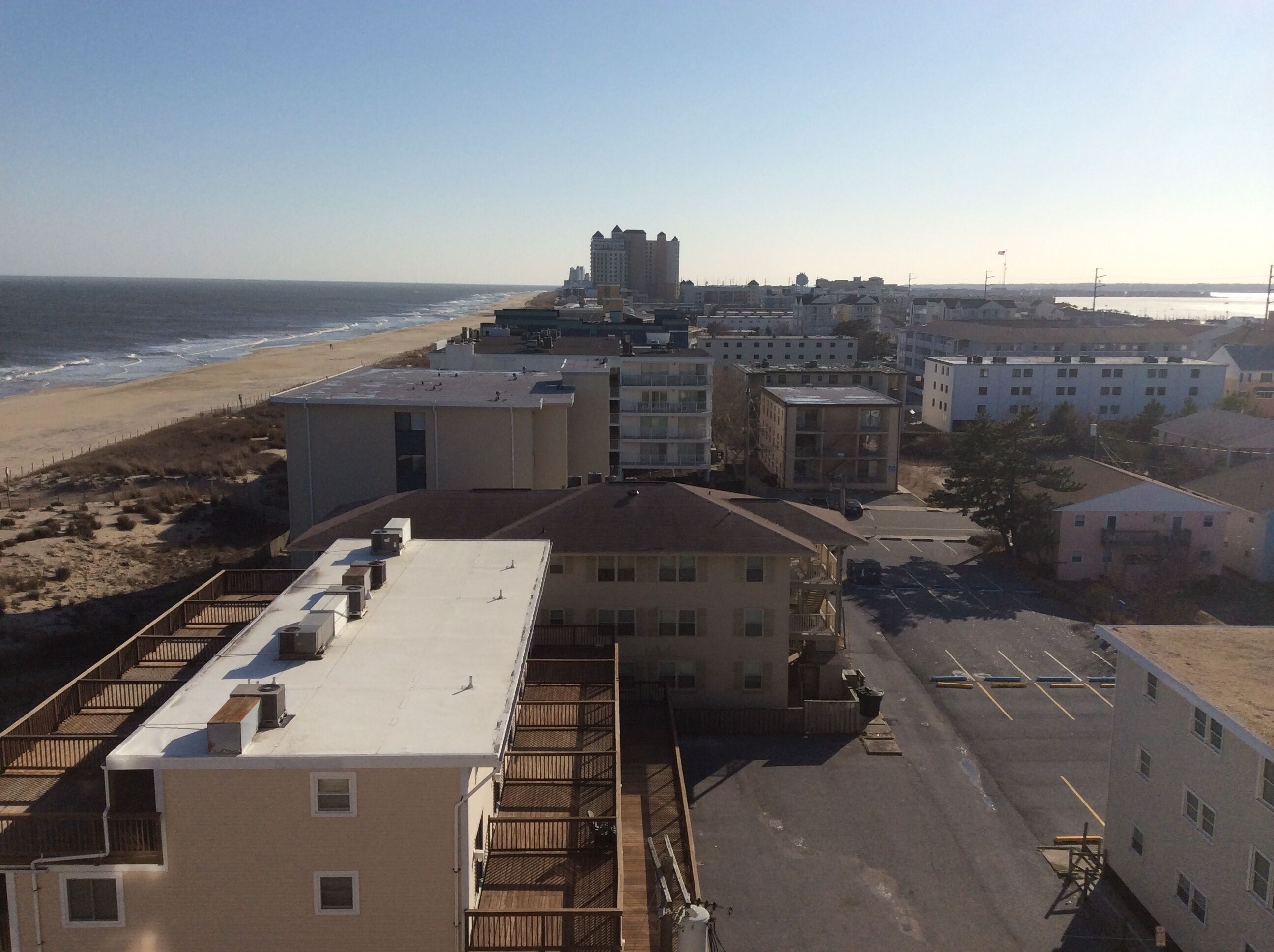 A coastal hotel with multiple buildings, a parking lot, and a beach in the background.