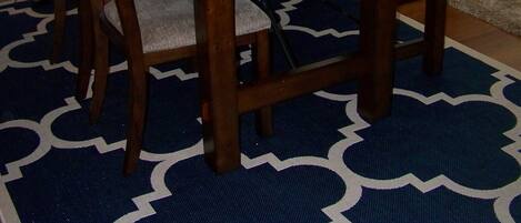 Een eethoek met een houten tafel en stoelen, een gekleurd tapijt en een zwarte leren bank.