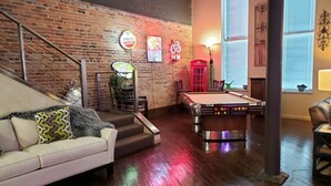 A cozy living room with a pool table, a white couch with patterned pillows, a brick wall, and neon signs. - Up to 50% off for limited time! Professionally Cleaned, Pool & Foosball Table (Nashville)