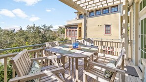 A wooden deck with a table and chairs, a pergola, and a building in the background. - Stylish Coastal Retreat | Large Balcony w/Views | Steps to Beach Club & Pools (Santa Rosa Beach)