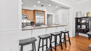 A modern kitchen with white cabinetry, a stainless steel refrigerator, a granite countertop, and bar stools. - Stylish Coastal Retreat | Large Balcony w/Views | Steps to Beach Club & Pools (Santa Rosa Beach)