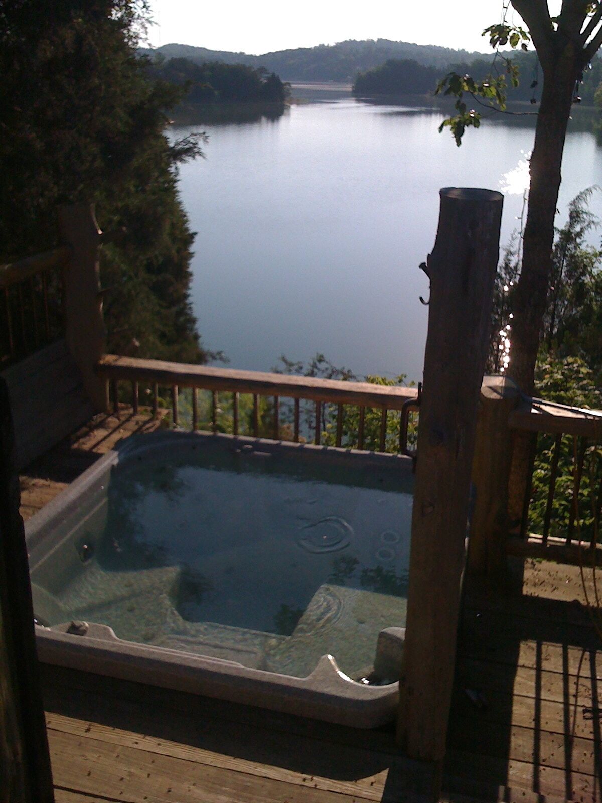 Een hottub op een houten terras met uitzicht op een meer en heuvels op de achtergrond.