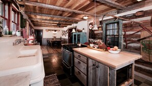 A rustic kitchen with wooden beams, a large wooden island, a vintage stove, and a farmhouse sink.