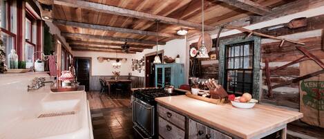 A rustic kitchen with wooden beams, a large wooden island, a vintage stove, and a farmhouse sink.