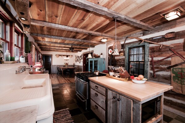 Une cuisine rustique avec des poutres en bois, un grand îlot central en bois, un poêle d’époque et un évier de style champêtre.
