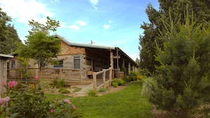 A rustic log cabin with a porch, surrounded by a well-maintained garden and tall pine trees.