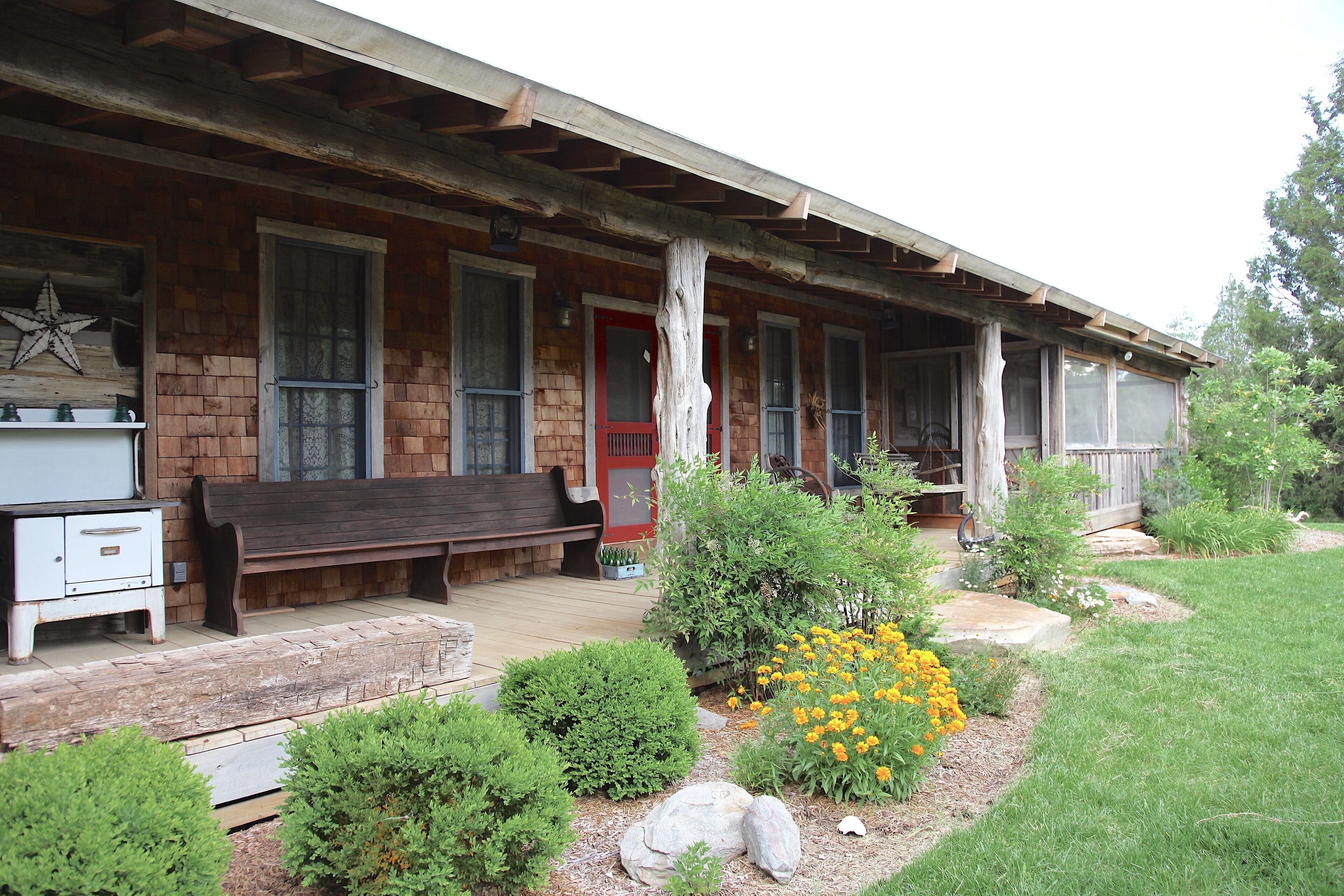 A rustic wooden house with a porch, a red door, and a bench.