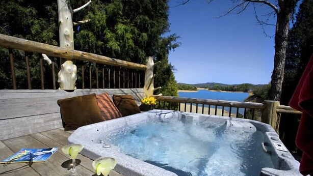 A hot tub on a wooden deck with a view of a lake.