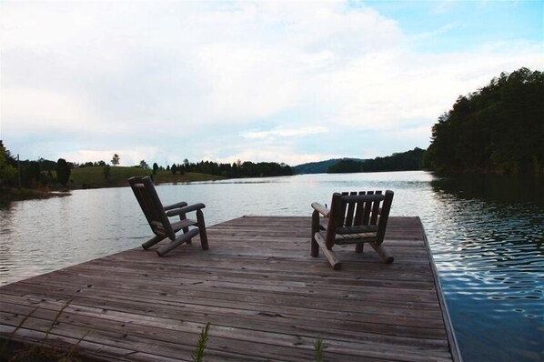 Relax on the dock with Adirondack chairs, surrounded by a serene forest and calm water.
