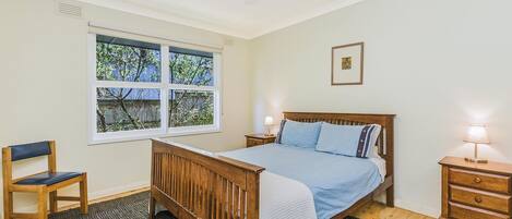 A bedroom with a wooden bed, a chair, a nightstand, and a window with a view of trees.