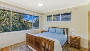 Ein Schlafzimmer mit großem Fenster, einem Bett, zwei Nachttischen und einem Deckenventilator.