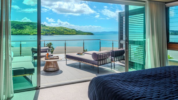 A balcony with a view of a lake and hills, furnished with a bed, sofa, and table. - Yacht Club Villa 33-Serenity-Ocean Views with Golf Buggy (Whitsundays)