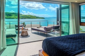 En balkon med udsigt over sø og bakker, møbleret med seng, sofa og bord.