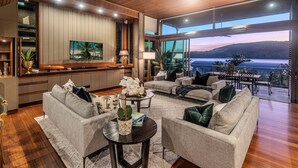 A spacious living area with a large window overlooking a body of water, a kitchen with wooden cabinets, and a comfortable seating arrangement. - Yacht Club Villa 33-Serenity-Ocean Views with Golf Buggy (Whitsundays)