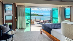 A modern hotel room with a large bed, a seating area with a view of the sea, and a balcony with a table and chairs. - Yacht Club Villa 33-Serenity-Ocean Views with Golf Buggy (Whitsundays)