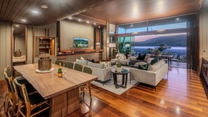 A spacious living area with a wooden dining table, comfortable seating, and a large window offering a view of the ocean. - Yacht Club Villa 33-Serenity-Ocean Views with Golf Buggy (Whitsundays)