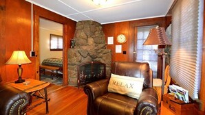 A cozy room with a stone fireplace, leather armchair, and a table with a lamp.