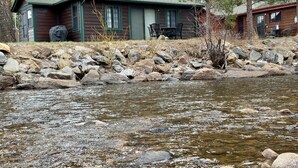 A cabin with a stone foundation, a small porch, and a dining area with outdoor furniture.