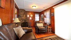 A cozy living room with a leather sofa, a fireplace, and a stone wall.