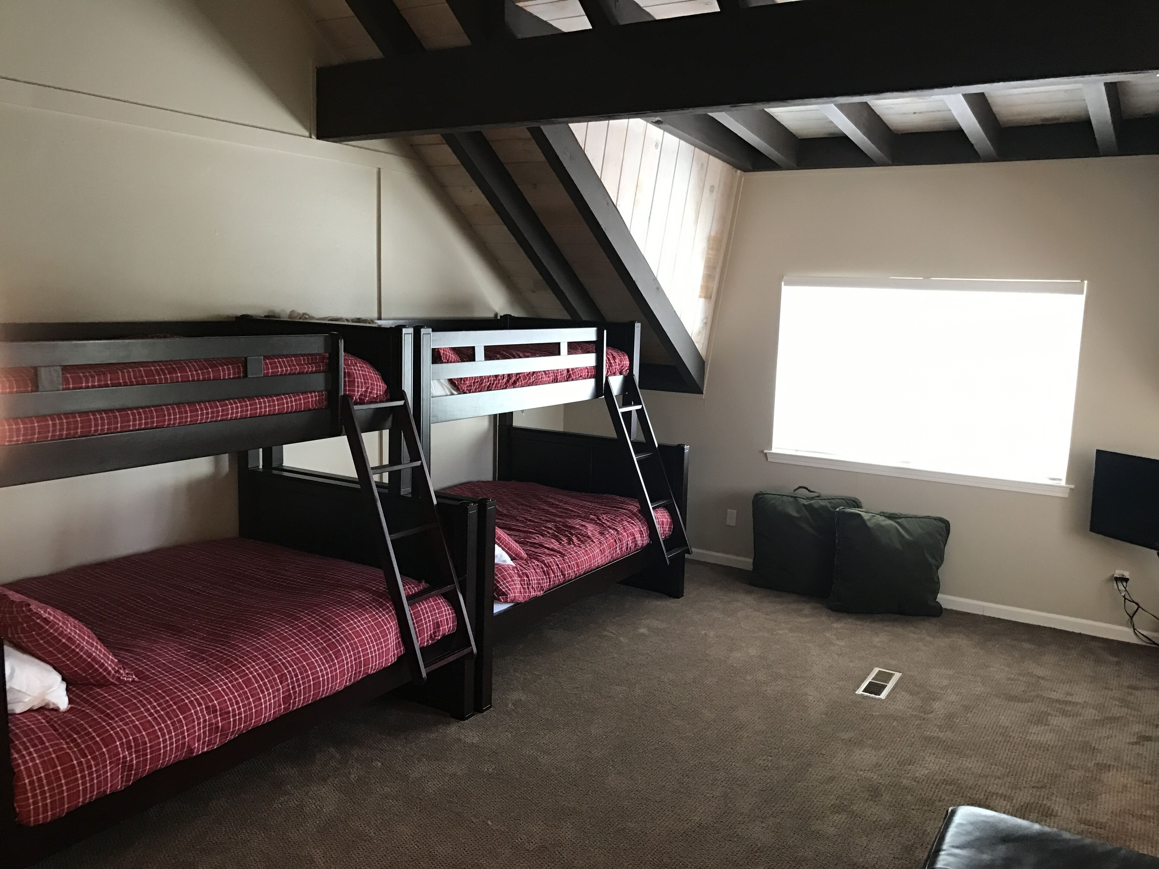 A dormitory room with bunk beds, a window, and a television.