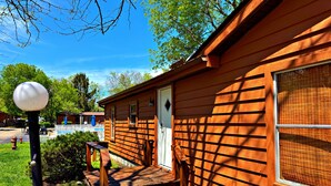 En stuga av trä med en veranda, en dörr och ett fönster med myggnät.