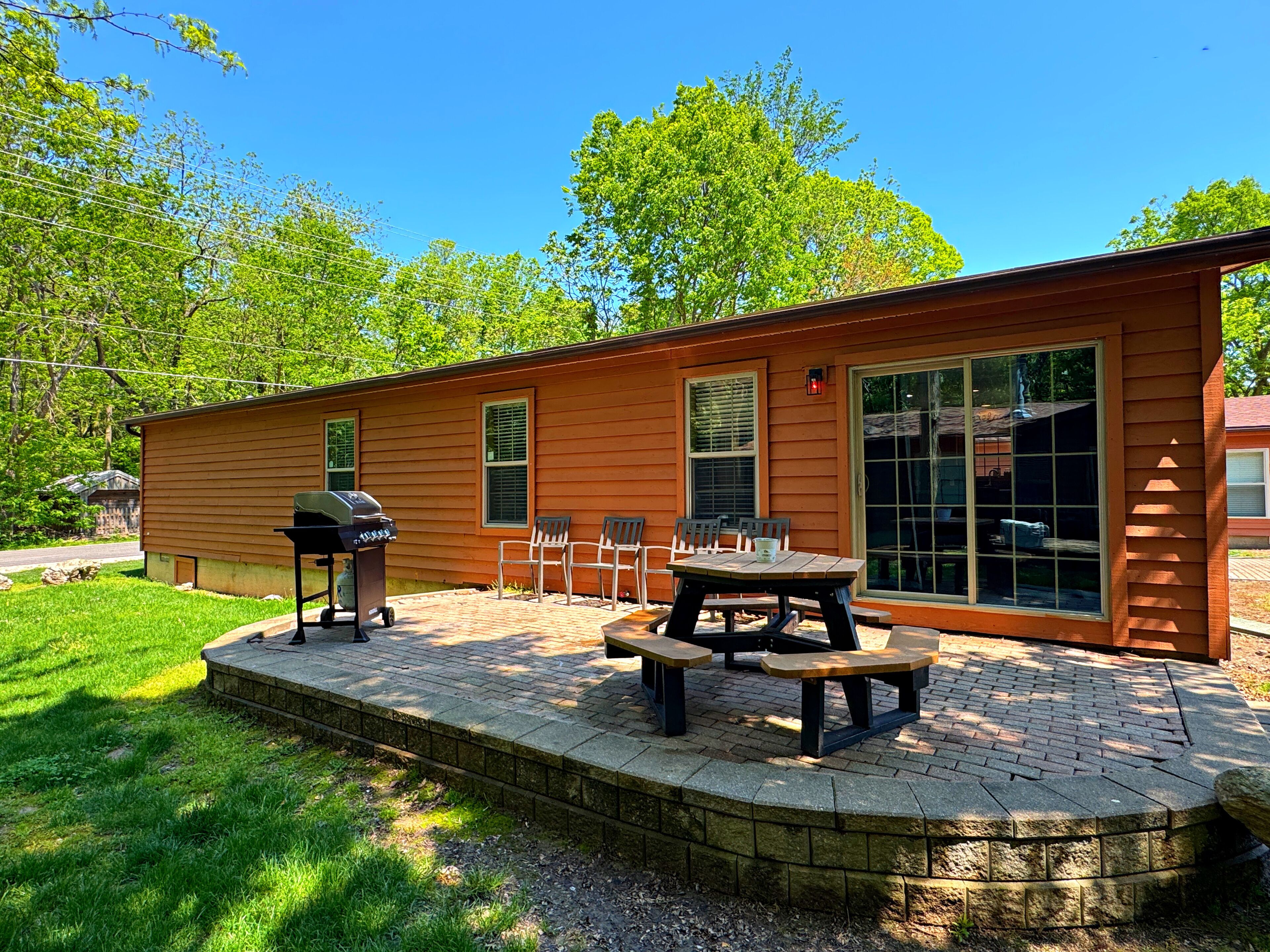 Een houten chalet met een terras, buitenmeubels en een barbecue.