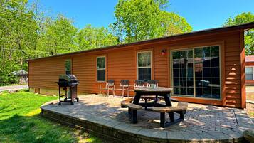 Een houten chalet met een terras, buitenmeubels en een barbecue.