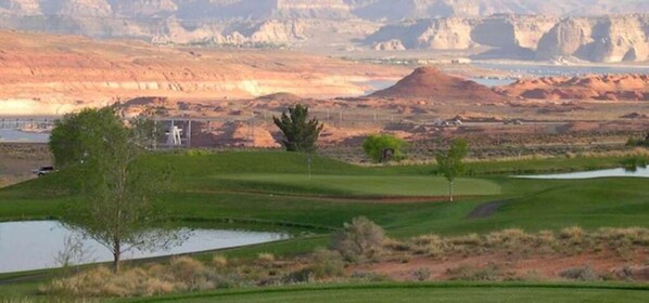 A golf course with a pond, trees, and a building in the background.