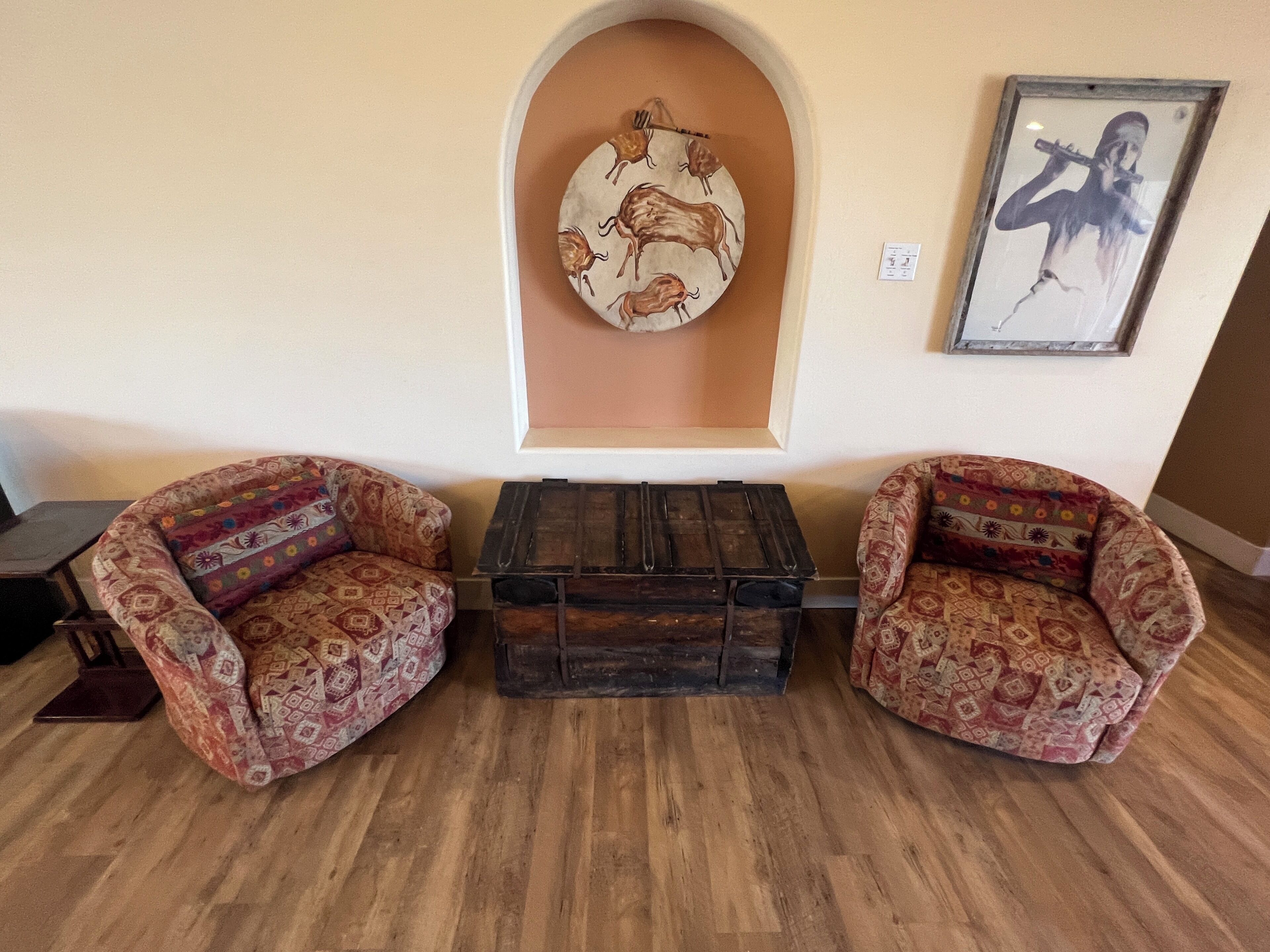 A room with two patterned armchairs, a small wooden table, and a wall-mounted artwork depicting a musical instrument.