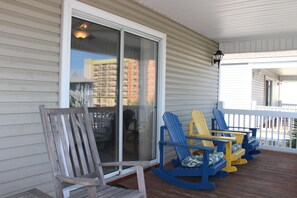 A porch with wooden chairs and a rocking chair, a sliding glass door, and a white railing. - 'BEACH BALL',Ocean Blvd,Great Location, Near Pier,Restaurants,See Reviews (Surfside Beach)