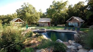 Ein Garten mit Swimmingpool, zwei kleinen Nebengebäuden und einem gepflegten Rasen.