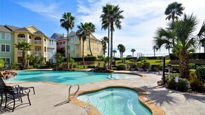 A swimming pool area with a hot tub, lounge chairs, and a view of multi-story buildings with balconies.