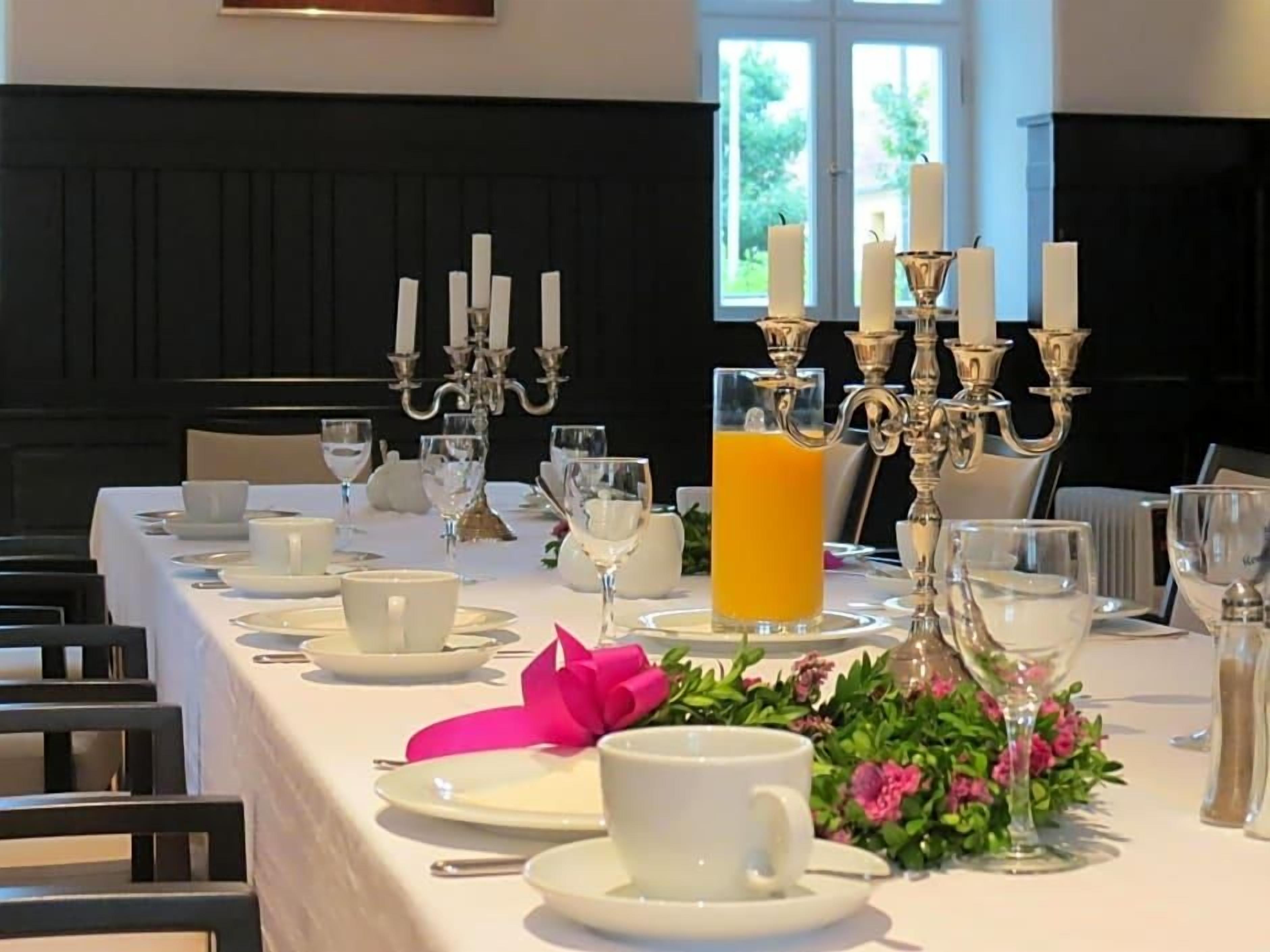 Ein Esstisch, gedeckt mit weißem Geschirr, ein Glas Orangensaft und eine rosa Schleife als Dekoration.
