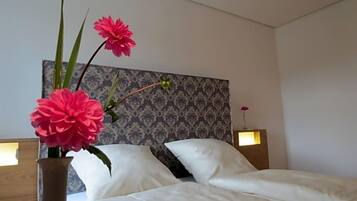 Ein Hotelzimmer mit einem Bett, weißer Bettwäsche, einer Blumenvase und einem Kopfende mit gemustertem Wandpapier.