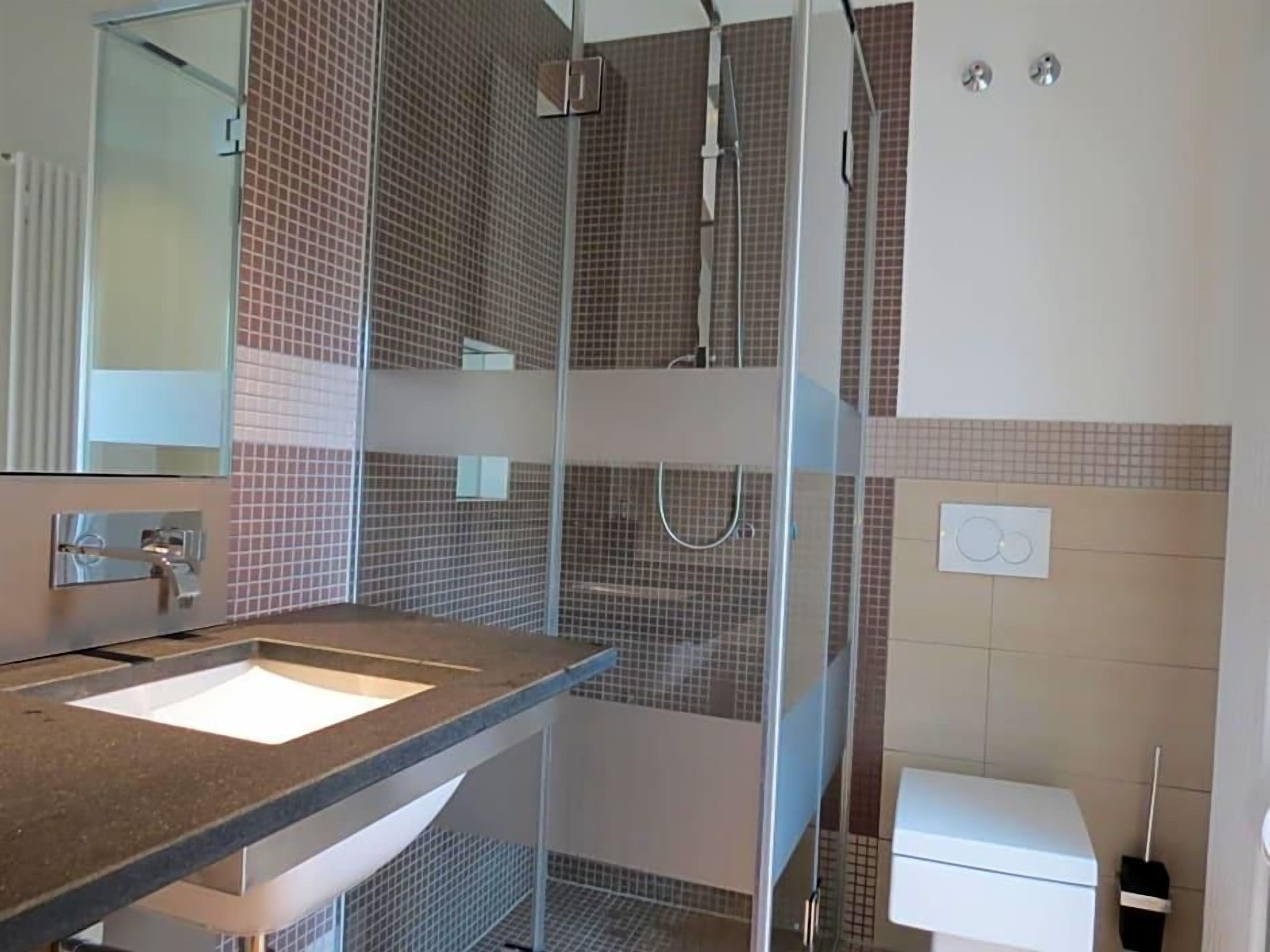 Ein Badezimmer mit Waschbecken, Spiegel, Dusche und Toilette.